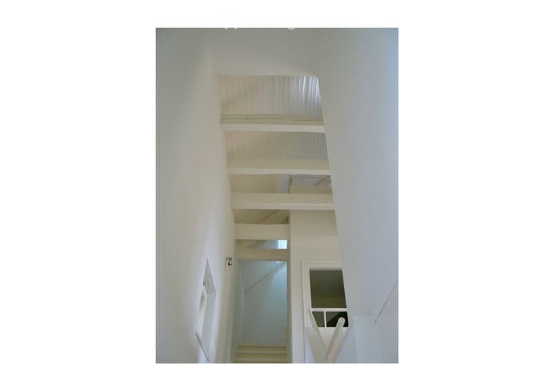 A modern, minimalist staircase with white wooden railings and open balustrades, leading upwards with visible steps and a bright, airy design.