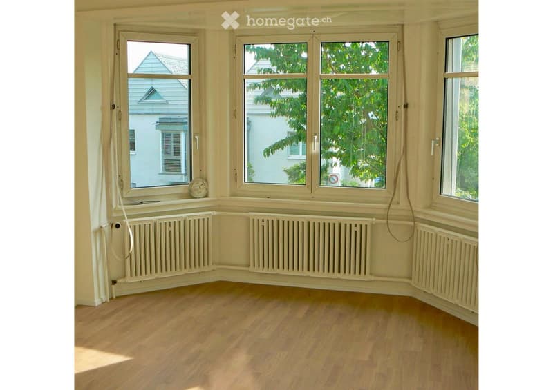 Empty room with wooden flooring, large windows, radiators, and natural light. No furniture or equipment present.