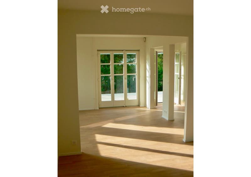 Empty room with wooden flooring, large windows, and open doors leading to an outdoor area.