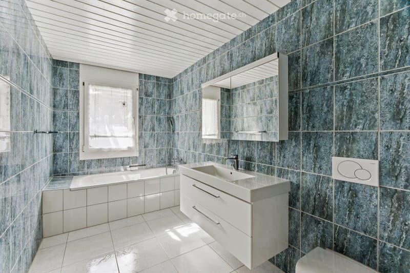 Modern bathroom with blue marble tiles, white fixtures, a bathtub, a sink with a cabinet, and a large mirror.