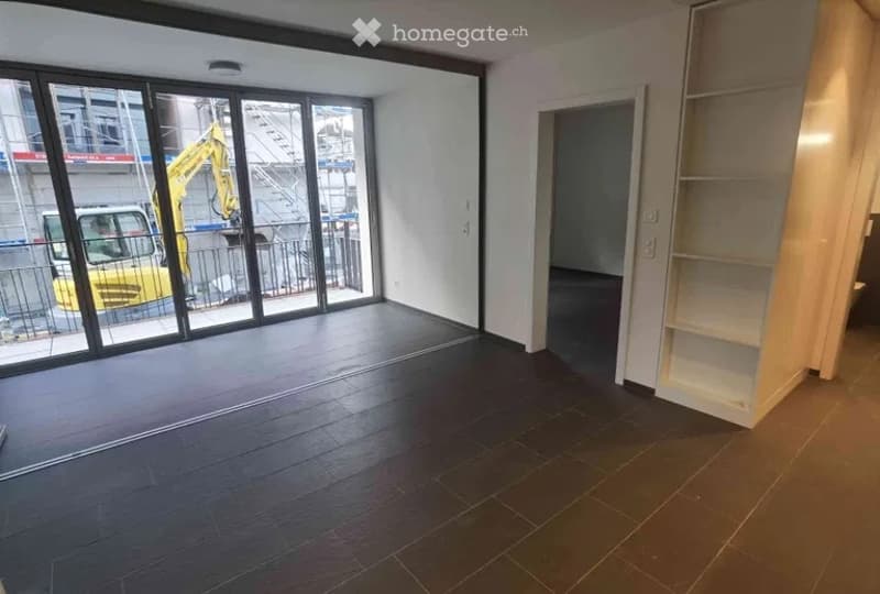Empty room with dark wooden flooring, large glass sliding doors leading to an outdoor area, and a built-in shelving unit on one wall.