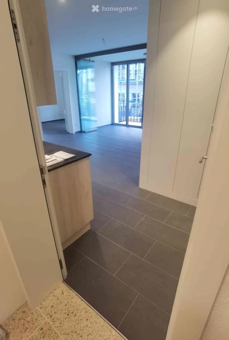 Empty hallway leading to a balcony area with tiled flooring and white walls.