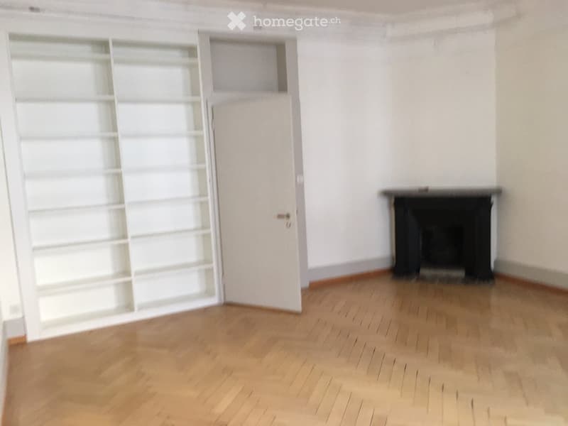 Empty room with wooden floor, white walls, fireplace, and a white shelf