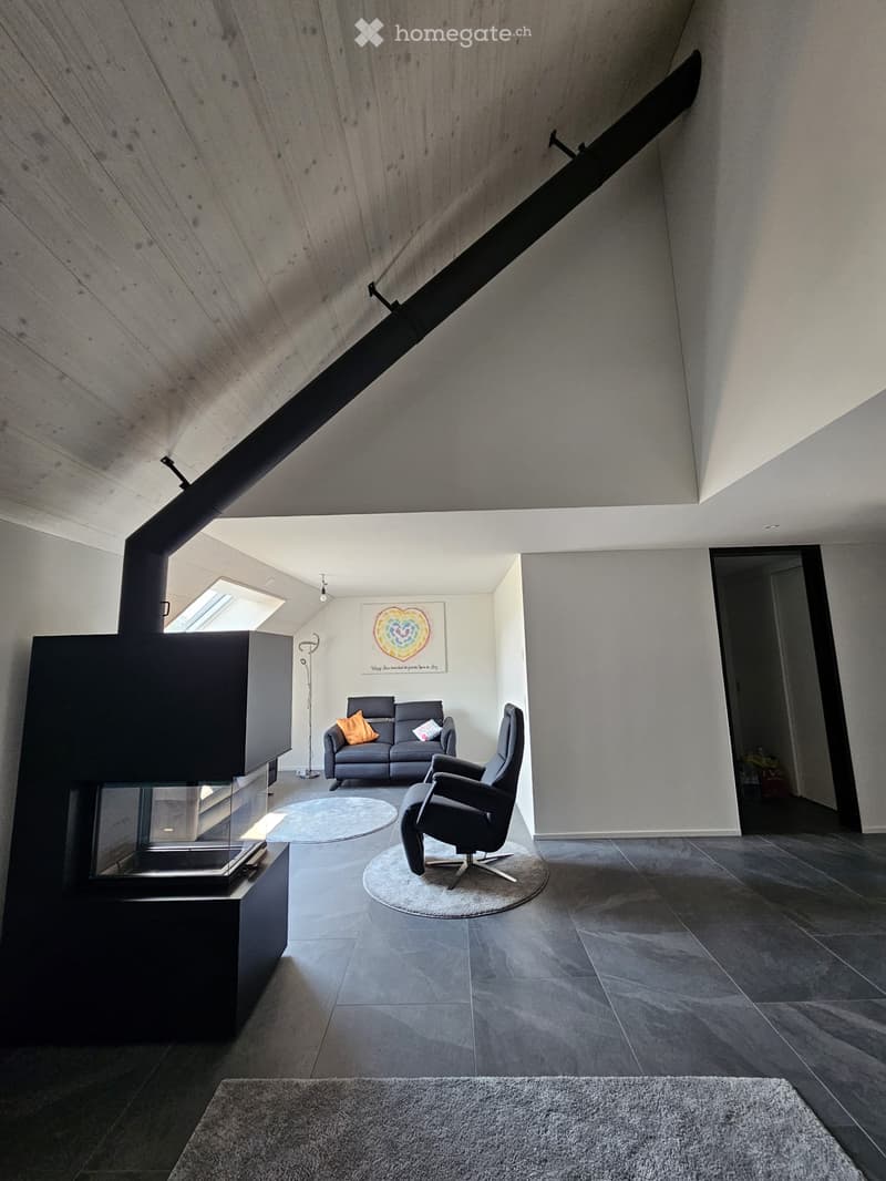 Modern living room with a fireplace, grey sofa, armchair, round rug, and a large abstract painting on the wall.