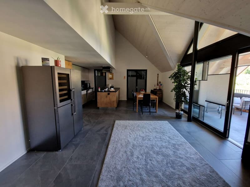 Modern open-plan living and dining area with a sleek refrigerator, wine cooler, kitchen island, dining table with chairs, and a cozy sofa near large windows.