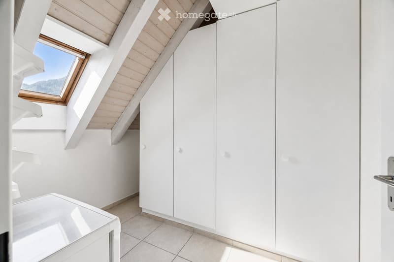 Bright, minimalist room with white walls, wooden slanted ceiling, built-in white cabinets, and a skylight window offering a scenic view.
