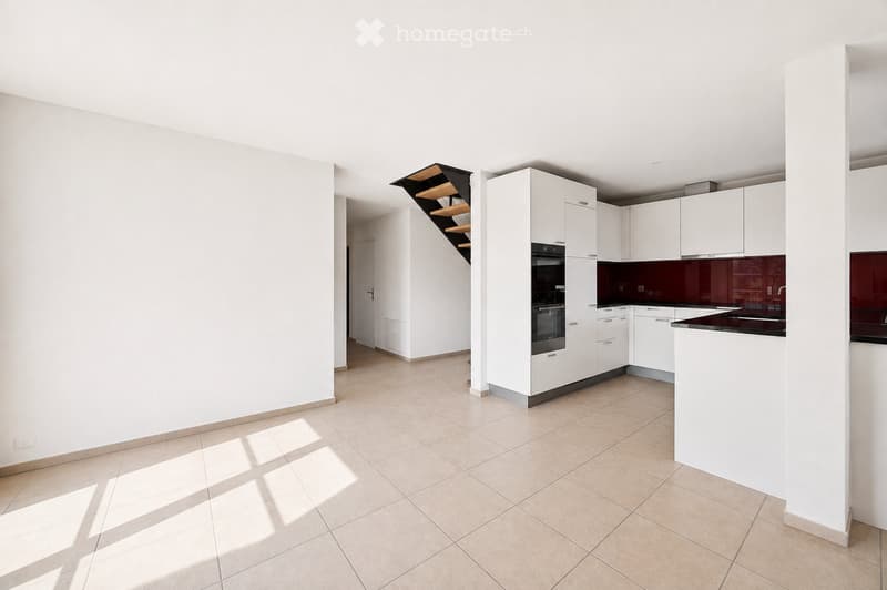 Modern, unfurnished kitchen with white cabinets, a built-in oven, and a dark countertop. The space features tiled flooring and natural light from a skylight above the staircase.