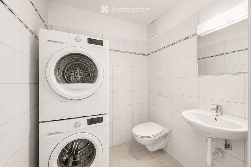 Modern bathroom with white tiled walls, a stacked washer and dryer, a toilet, and a sink with a mirror above it.
