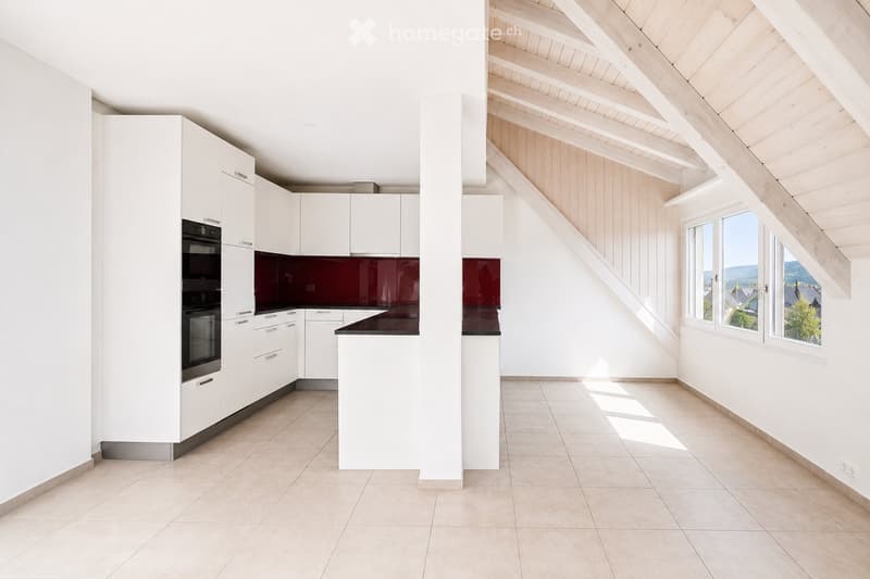 Modern kitchen with white cabinets, a dark red backsplash, and a black countertop. The adjacent room has wooden beams and large windows offering a scenic view.