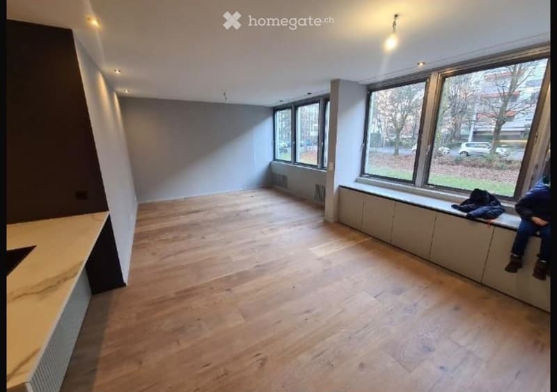 Empty room with wooden flooring, large windows, and built-in bench seating along one wall.