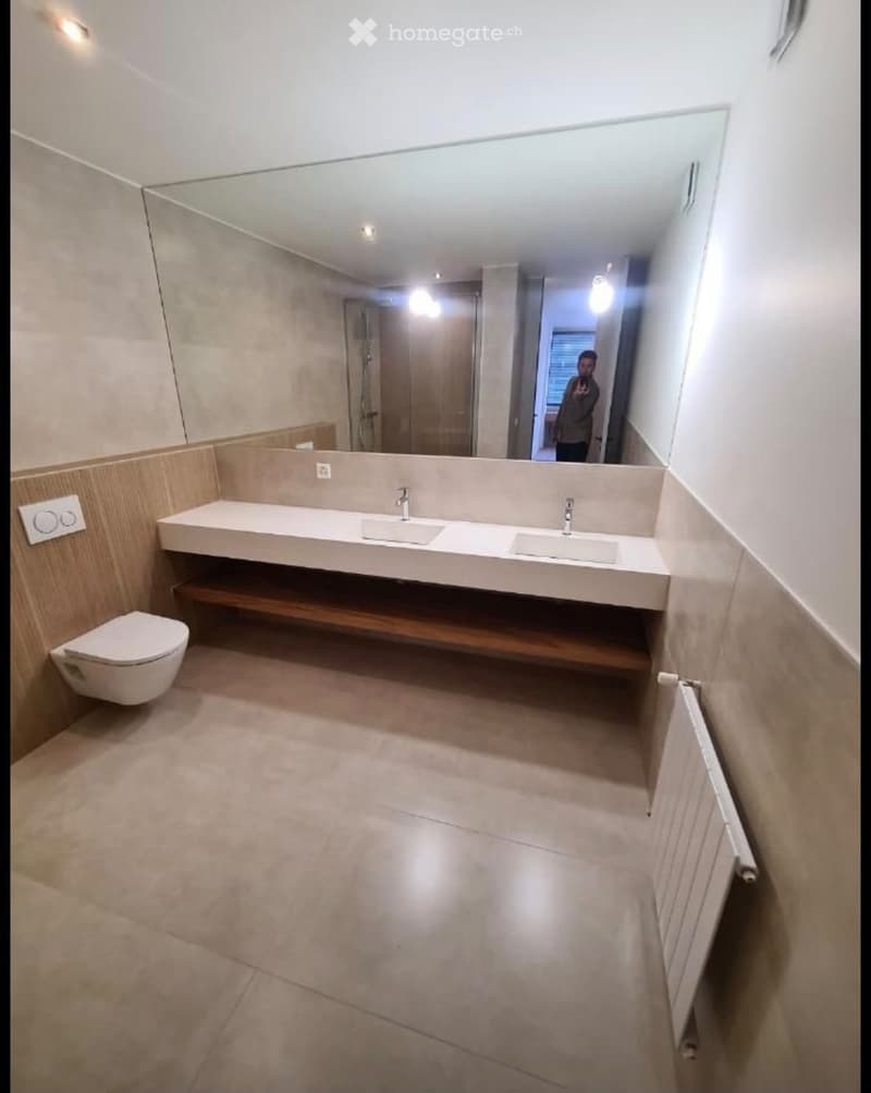 Modern bathroom with beige tiles, double sink, toilet, large mirror, and radiator.