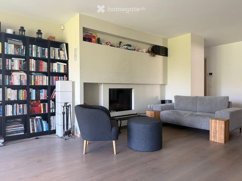 Modern living room with a grey sofa, armchair, ottoman, coffee table, bookshelf, and fireplace.