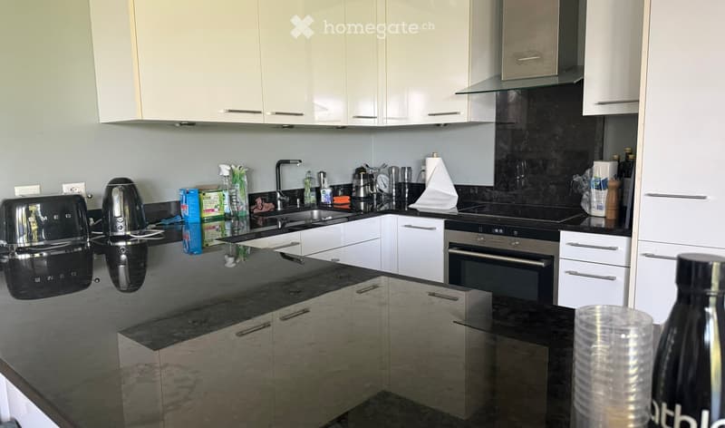 Modern kitchen with white cabinets, black countertops, stainless steel appliances, and a central island.