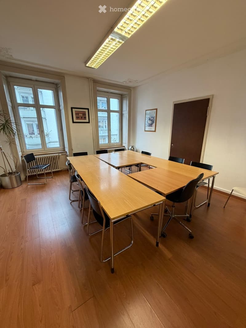 conference room, wooden desk, black chairs, windows, radiator, pictures on the wall, potted plant, wooden floor
