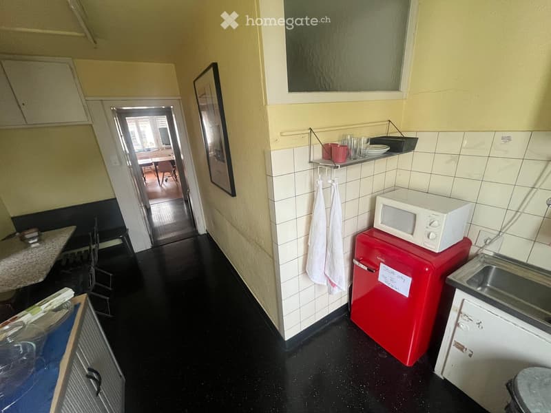 small kitchen, wooden floor, white tiles, fridge, microwave, sink, hanging towels
