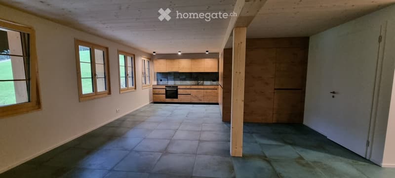 Modern kitchen with light wooden cabinets, stainless steel oven, and tiled floor. Large windows provide natural light.