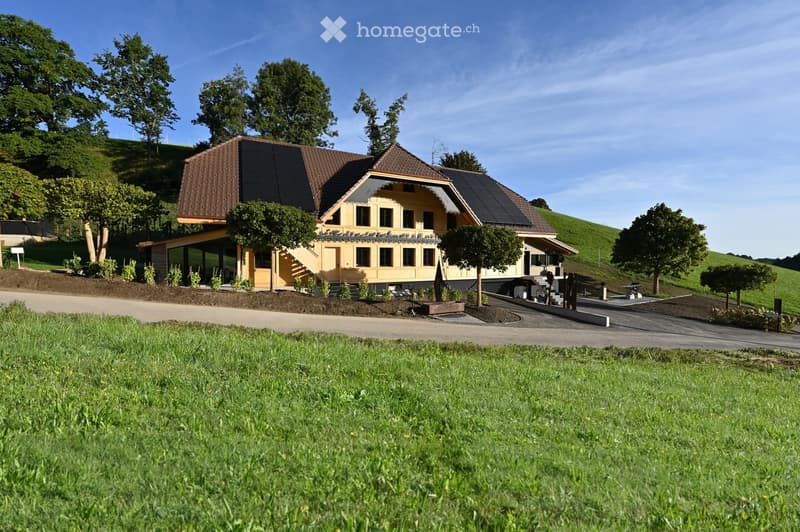 Modern two-story house with solar panels on the roof, surrounded by a well-maintained lawn and trees.