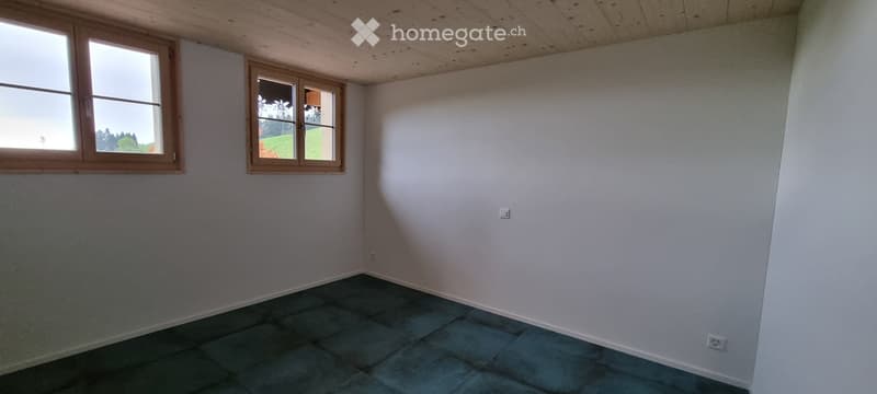 Empty room with light wooden ceiling, white walls, and dark tiled floor. Two windows with wooden frames provide natural light.