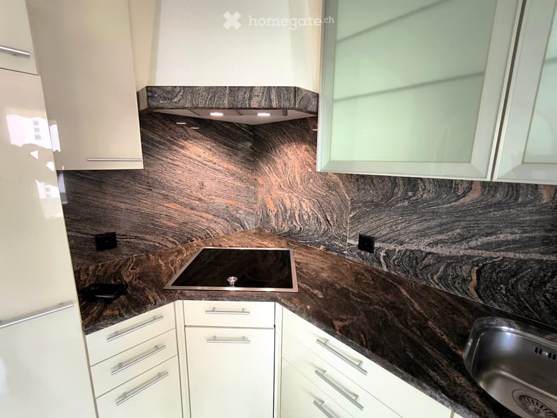 Modern kitchen with white cabinets, dark marble countertops, and an induction stove. Features a stainless steel sink and sleek, contemporary design.