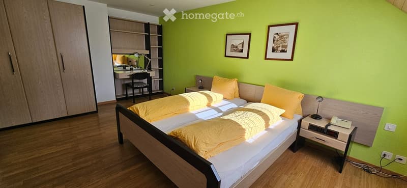 Bright bedroom with green walls, double bed with yellow bedding, nightstand, desk with chair, and framed pictures on the wall.