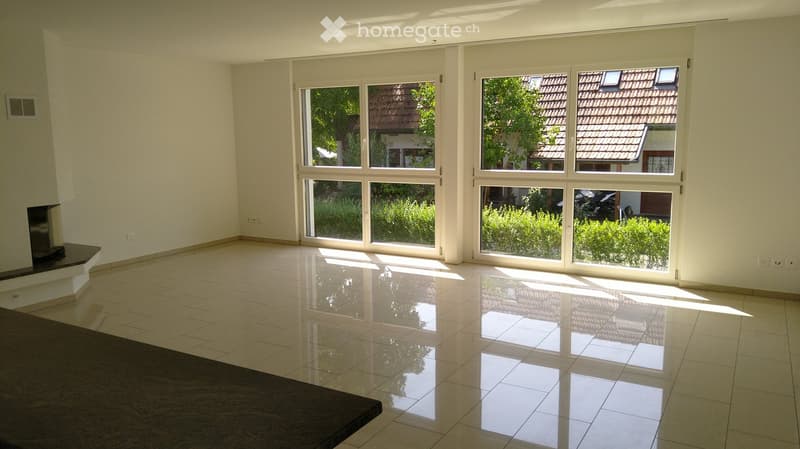 Empty room with large windows, tiled floor, and a small fireplace area.