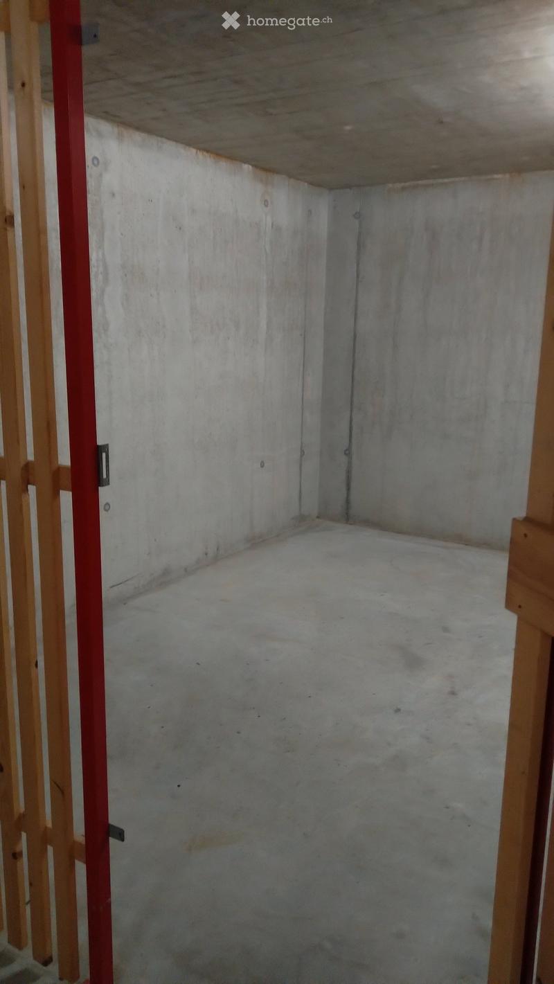 Empty room with bare concrete walls and floor, exposed wooden framing on the left side, and a red metal support beam.