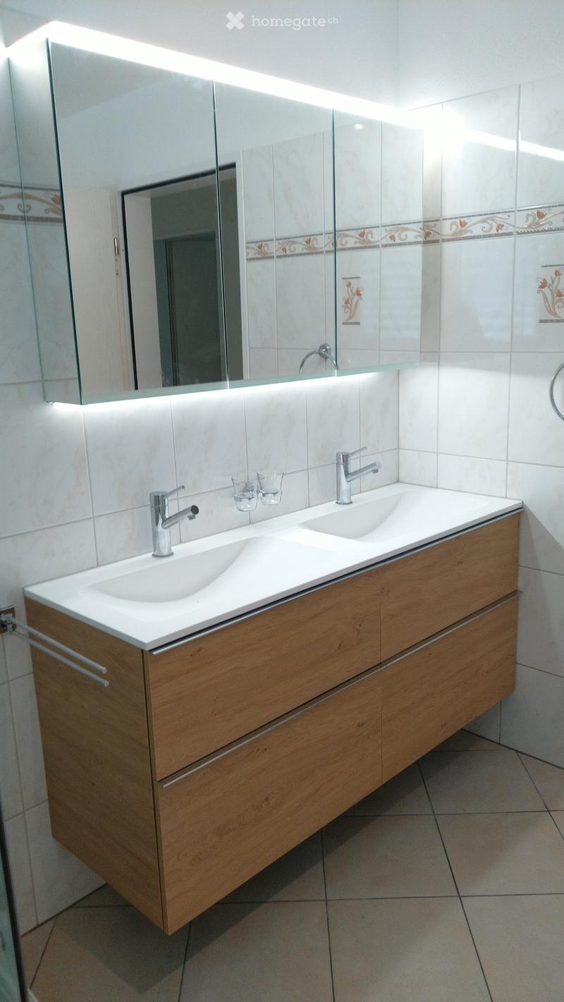 Modern bathroom with a double sink vanity, wooden cabinet, chrome faucets, and a large mirror with built-in lighting.