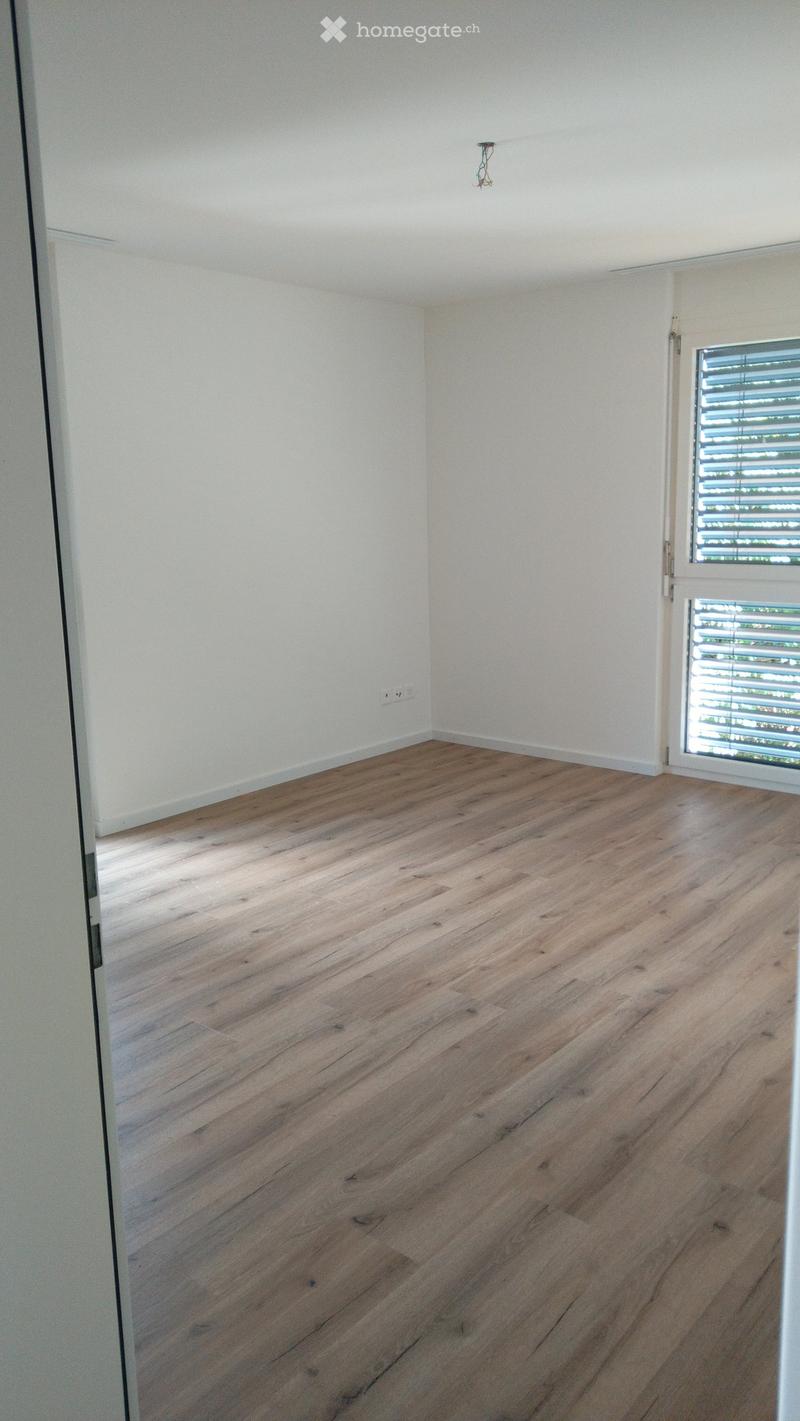 Empty room with light wooden flooring, white walls, and a large window with blinds.