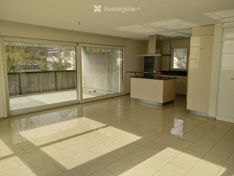 Empty kitchen with tiled floor, large sliding glass doors leading to a balcony, and a modern kitchen island with built-in appliances.