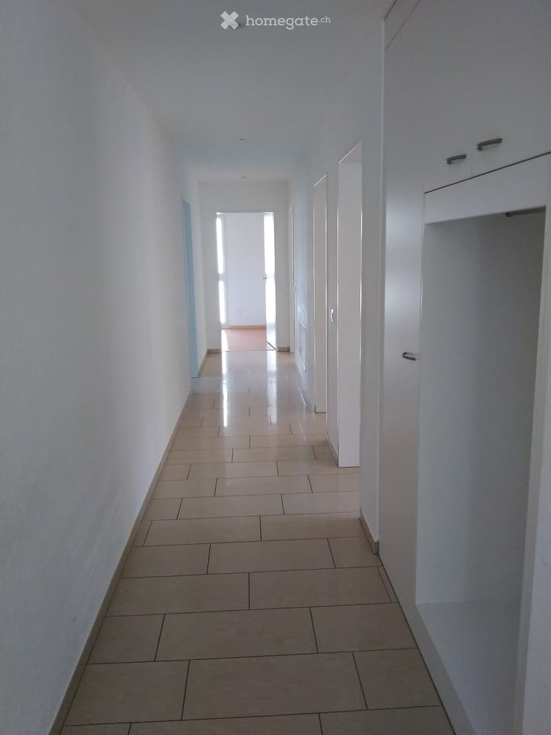 Empty hallway with tiled floor, white walls, and a closed door at the end.