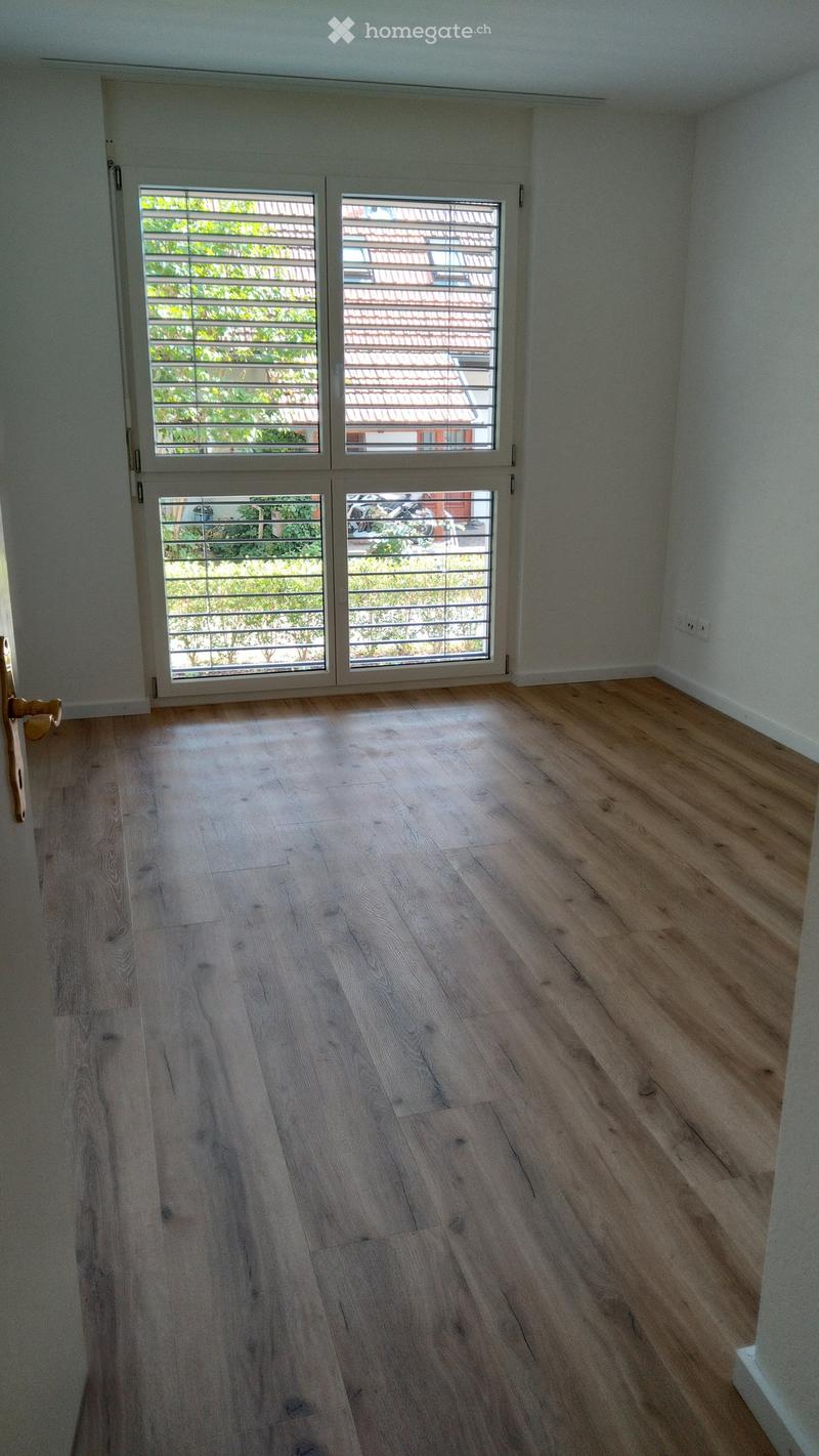 Empty room with light wooden flooring, white walls, and large sliding glass doors leading to a balcony or outdoor area.