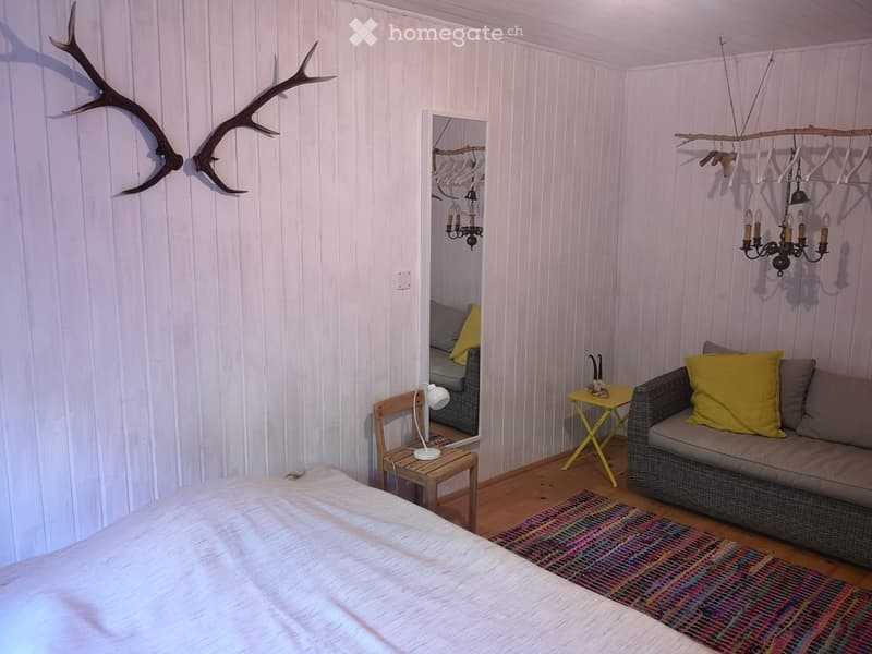 bedroom with bed, mirror, sofa, table, wooden chair, wooden floor, chandelier, deer antlers on wall