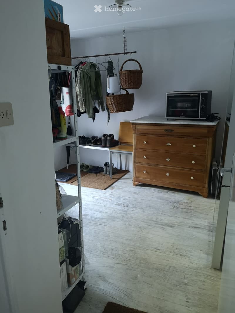 A small closet room with storage, shoes, a microwave, and a chair.