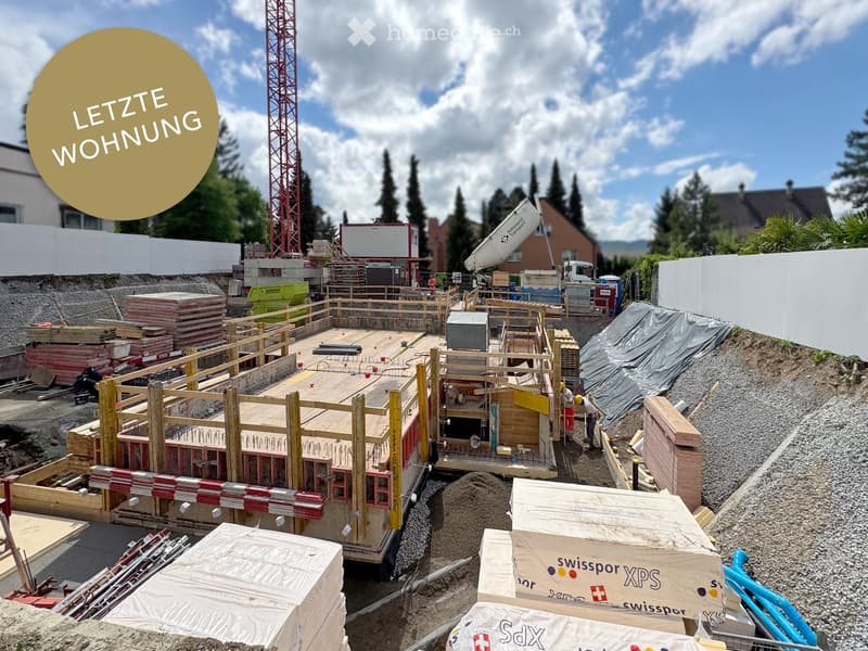 Construction site with wooden framework, stacked materials, and a crane in the background.