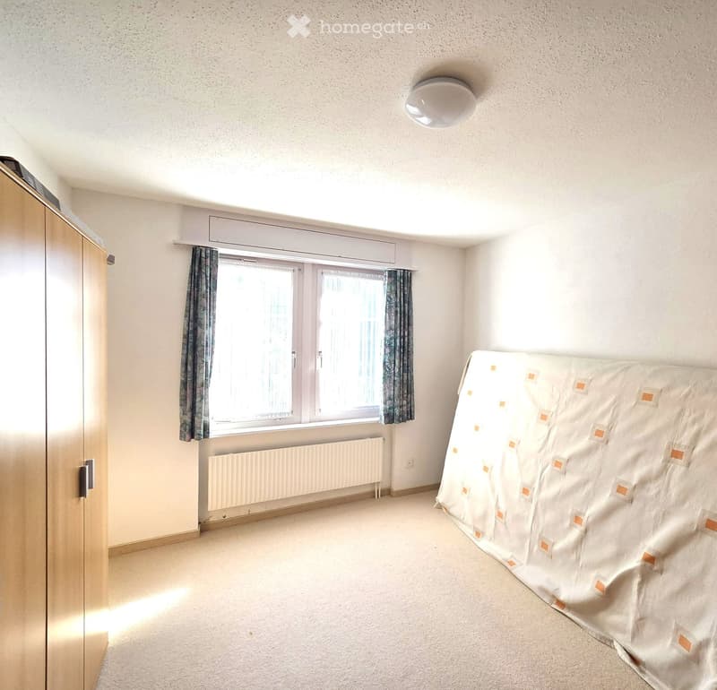 Bedroom with a bed, wardrobe, window with curtains, radiator, and a ceiling light fixture.