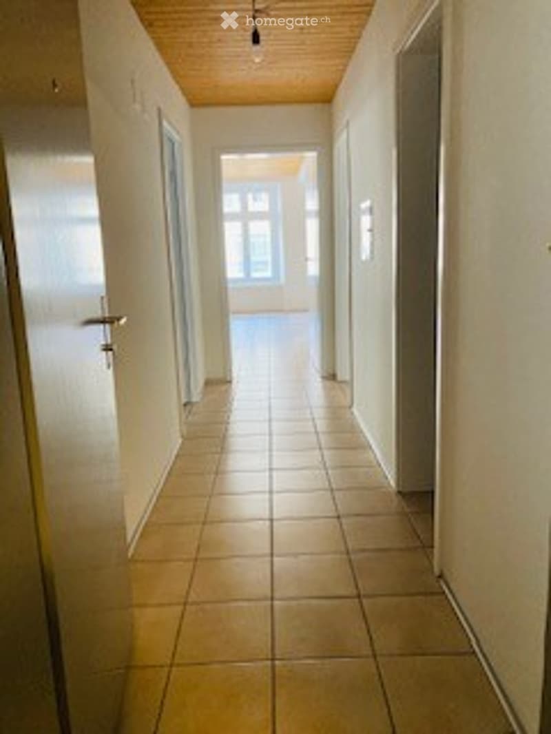 Empty corridor with tiled flooring, three doors, and an opening leading to a room with a window.