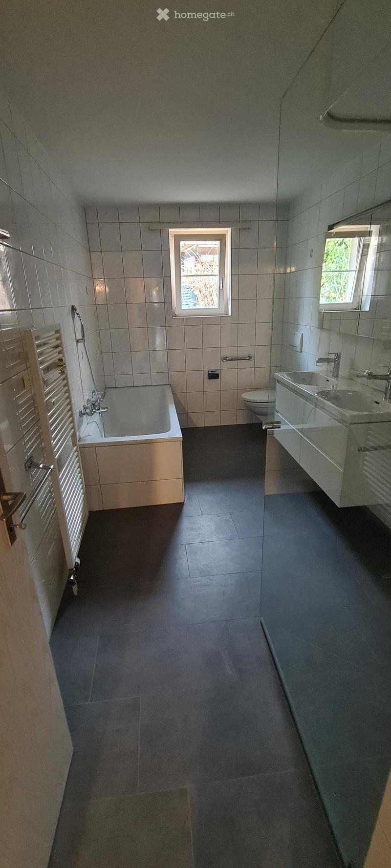 modern bathroom with bathtub, separate toilet, two sinks, wall mounted heating, windows