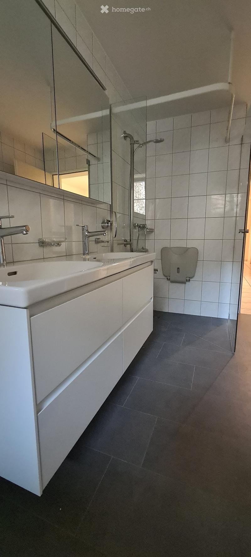 white bathroom, tiles, white sinks, shower with glass door, mirror, toilet