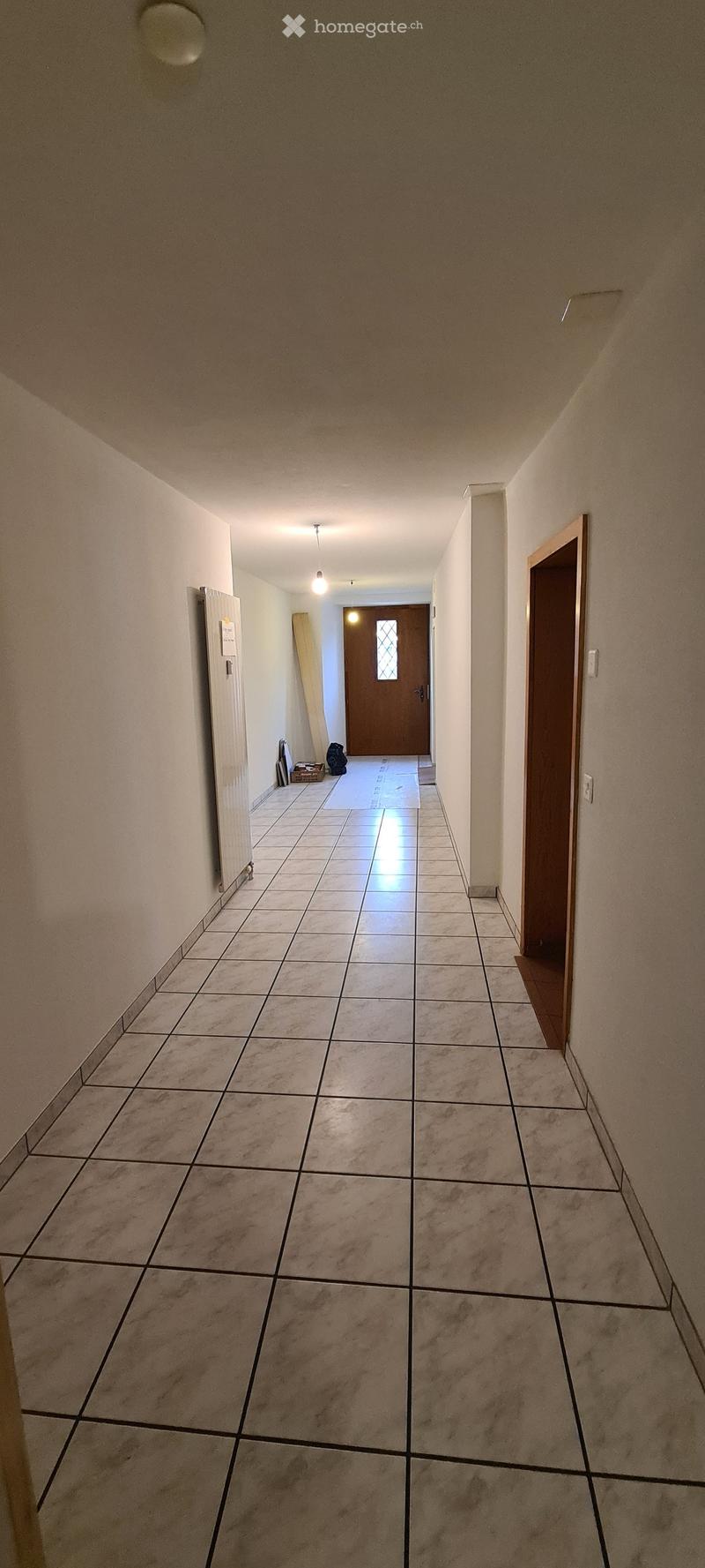 white tiled floor, white walls, ceiling with lights, two closed wooden doors, wooden structure leaning against the wall