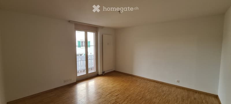 Empty room, wooden floors, sliding glass door to balcony, white walls, power outlets