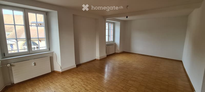 Large empty room, large windows, white walls, wooden floor, radiators