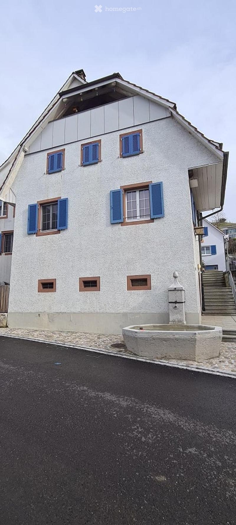 3 story house, white painted walls, blue shutters, 2 small balconies, chimney, stone fountain