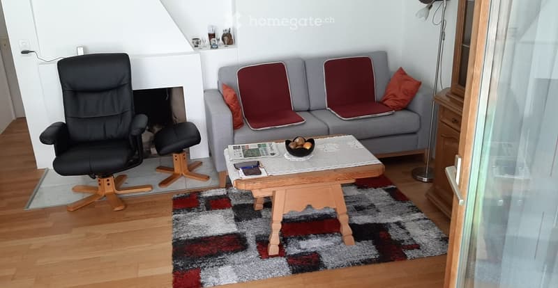 Living room with a grey sofa, wooden coffee table, black leather chair, fireplace, and a patterned rug.