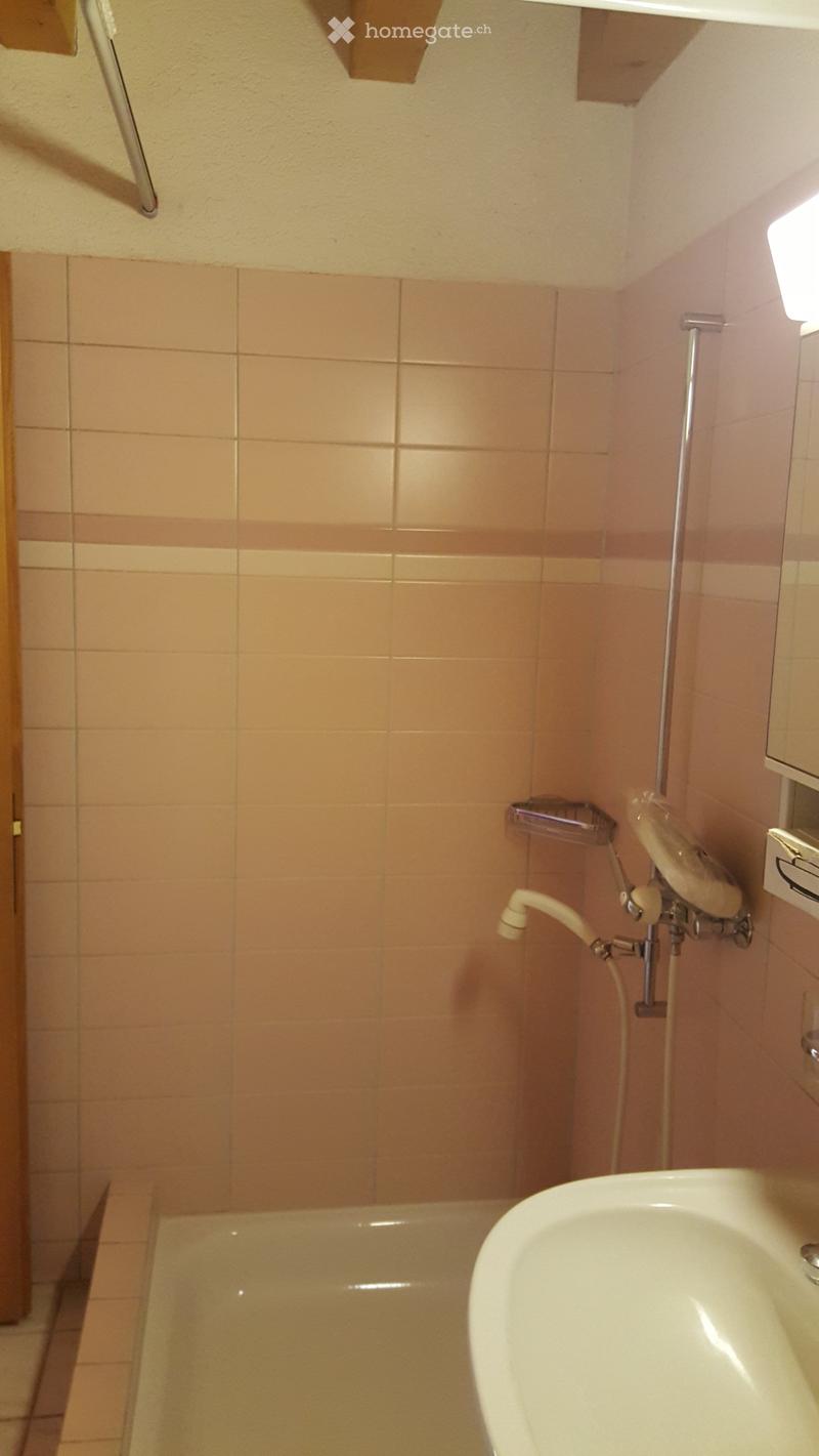 Bathroom with beige tiles, a bathtub, a sink, and a showerhead mounted on the wall.
