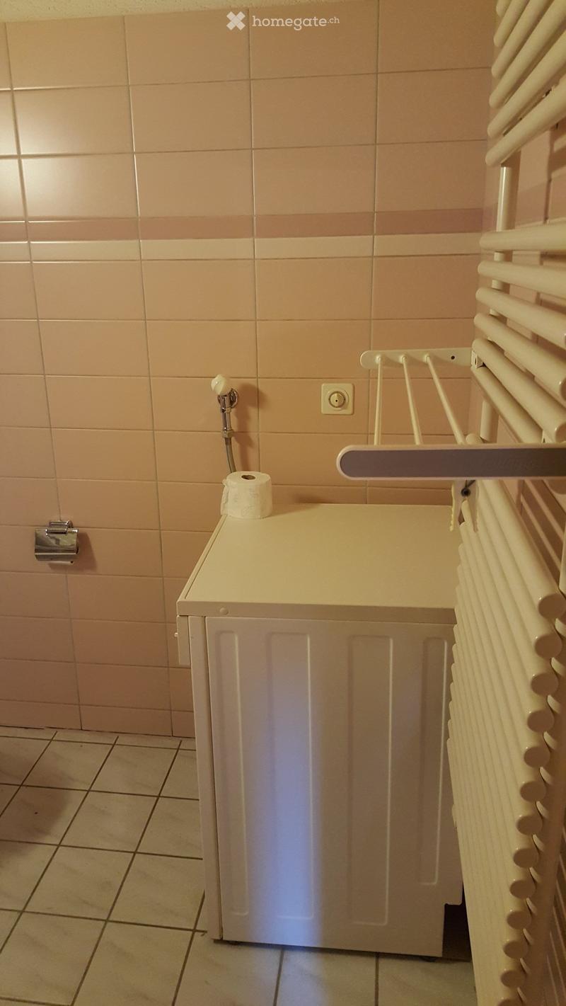 A small bathroom with beige tiled walls and floor, featuring a toilet, toilet paper, a radiator, and a faucet.