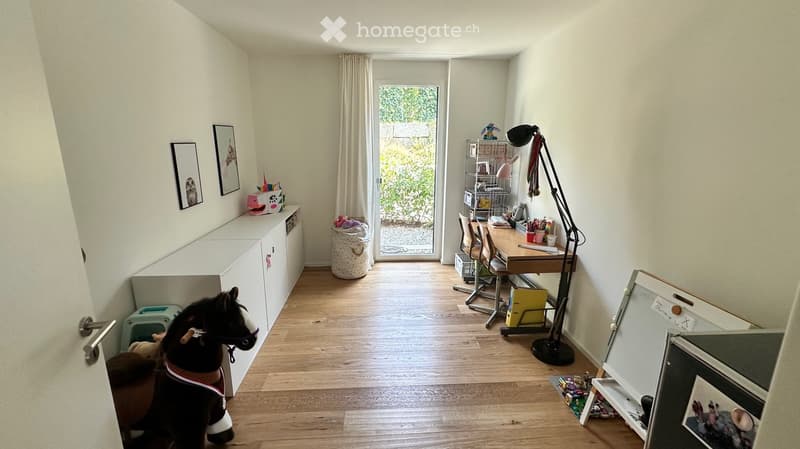 A well-lit room with wooden flooring, a toy horse, a desk with a chair, a floor lamp, a cabinet, and various toys and decorations.