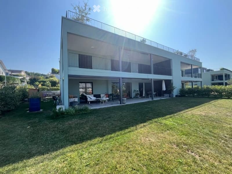 Modern two-story house with large balconies, large windows, and a well-maintained lawn in front.