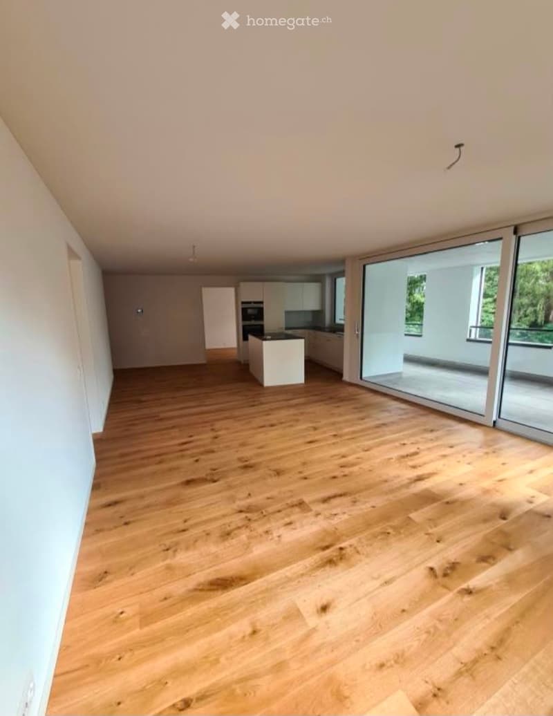 Empty room with wooden flooring, large windows, and a view of the balcony area.