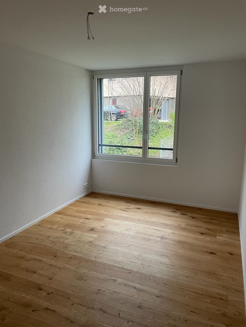 Empty room with wooden flooring and large window offering view of outdoor area.