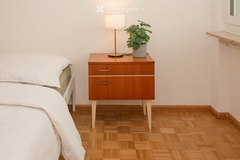 A bedroom with a bed, nightstand, lamp, and potted plant.